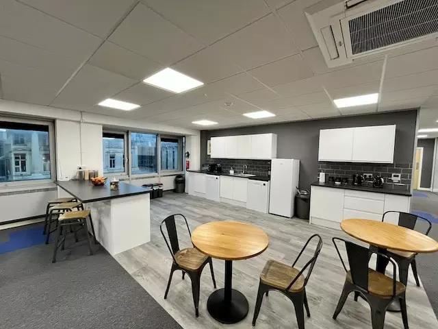 Kitchen Area at Barts House Office Space in Brighton with two round wooden tables and two wooden black framed chairs in front of black and white kitchen cabinets.