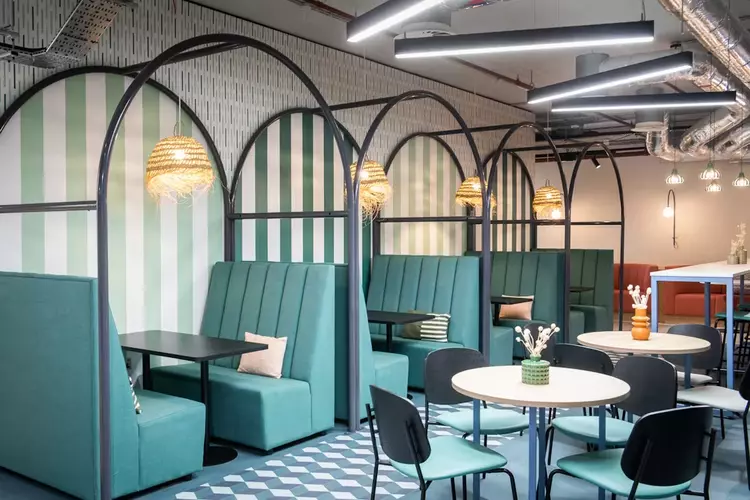 Breakout Space and Coworking area at Runway East Brighton, with four teal couch booths and black tables and a sage green and white stripped wallpaper in the background