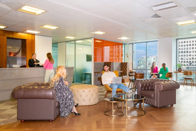 Reception Area at Servcorp Canary Wharf offices with people sitting in the waiting area equipped with brown leather couches and booths