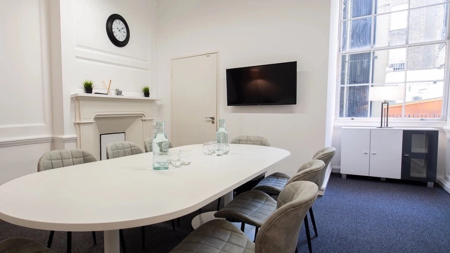 Large meeting room at Boutique Workplaces Henrietta Street with a TV screen and a large window in the backgroun and a clock on the wall