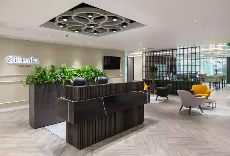 Reception Area at Gilbanks 11 York Street showcasing a wood panelled receptionist desk with two black leather office chairs, alongside it are single seater couches one nude, one is orange and one is green